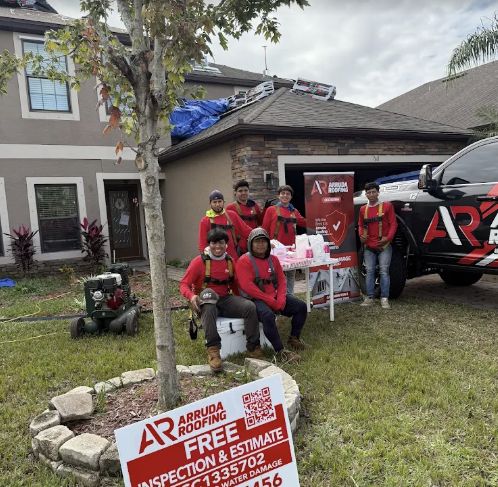 Roofing crew posing outside a house with company truck, inspection sign, and roofing materials on the roof