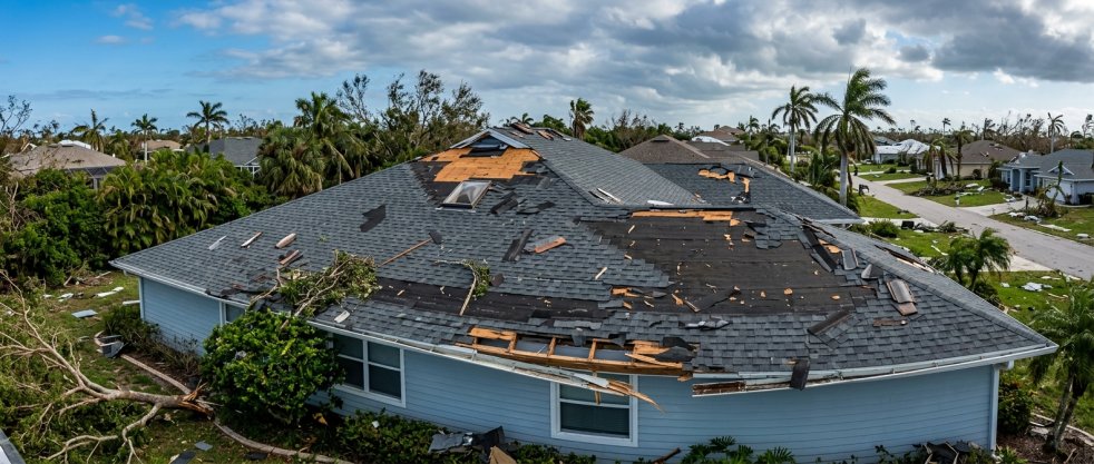 Storm-damaged house roof with missing shingles and debris in a suburban neighborhood after severe weather