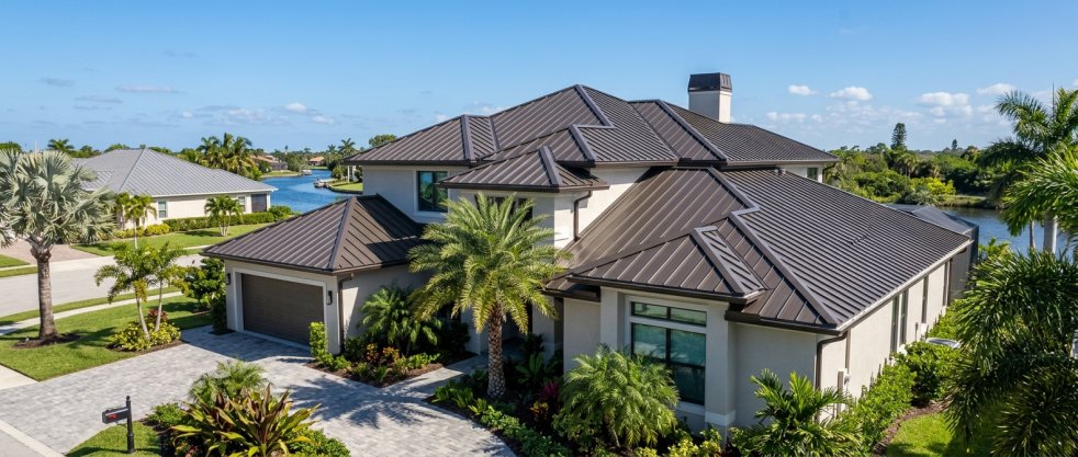Luxury home with dark metal roof in a tropical waterfront neighborhood with palm trees and landscaped yard